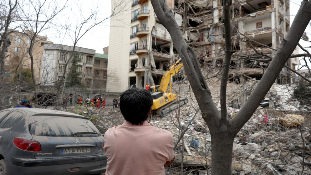 أحد السكان يراقب رجال الإطفاء الإيرانيين وهم يزيلون الأنقاض من مبنى سكني مدمر في شمال طهران 