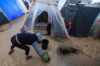 فلسطيني نازح يستخدم دلوًا لإزالة المياه من خيمة غمرتها الأمطار الغزيرة في رفح (أ.ف.ب)